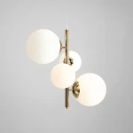 Lampa wisząca Bloom 4-punktowa w kolorze złotym z czterema okrągłymi, mlecznymi kloszami. Produkt zawieszony na cienkim przewodzie, z centralnym metalowym słupkiem. Tło jasnoszare, bez dodatkowych elementów.