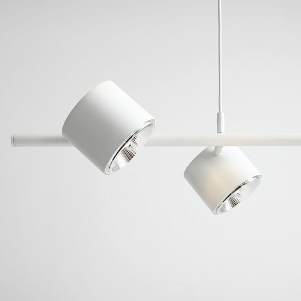 Lampa wisząca 4-punktowa w kolorze białym, z dwiema okrągłymi, ruchomymi głowicami na prostokątnej belce. Całość zawieszona na cienkim przewodzie. Elementy wykonane z metalu, z przezroczystymi kloszami, umieszczone na jasnym tle.
