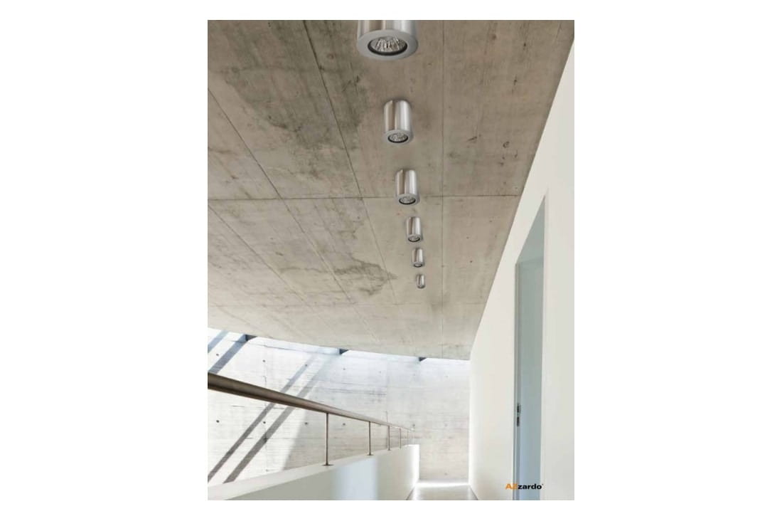 Lampa sufitowa Boris 1-punktowa w kolorze aluminium, zamontowana na stropie o betonowej powierzchni. Widoczna z boku, podkreślająca nowoczesny design i minimalistyczny styl, w otoczeniu jasnych ścian i schodów.