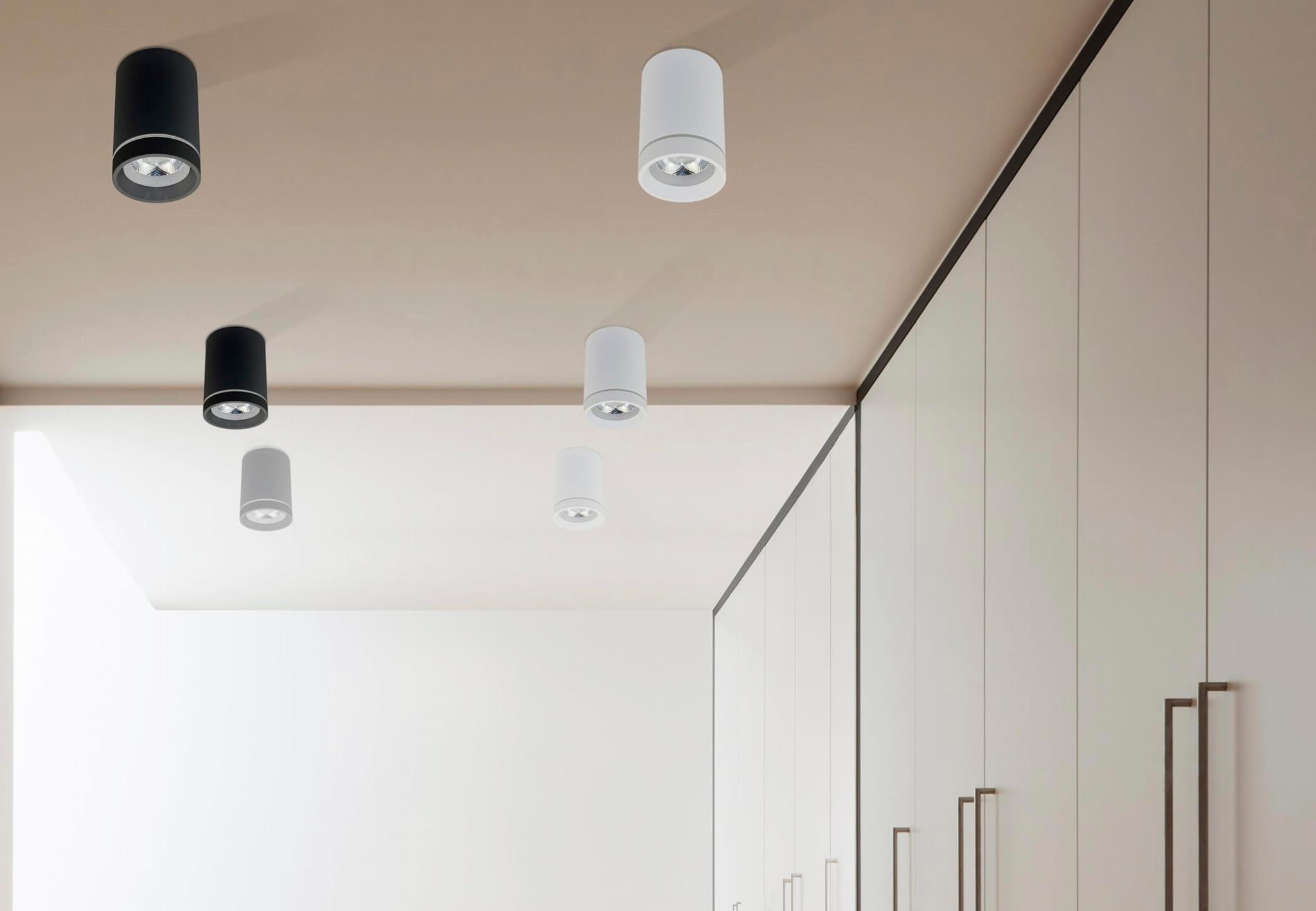 Biała lampa sufitowa LED Bill 1-punktowa, cylindryczna, z widoczną oprawą na sufit. Zawieszona na jasnym tle, w towarzystwie czarnych lamp. Prosty design, idealna do nowoczesnych wnętrz.