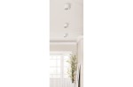 Biała lampa sufitowa Eco Alix New 230V w formie jednego punktu, montowana na suficie. Okrągła obudowa z przezroczystym kloszem, umieszczona w nowoczesnym wnętrzu z jasnymi ścianami i rośliną w doniczce.