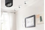 Lampa sufitowa Alix 230V w kolorze białym, jednopunktowa, z metalowym kloszem, zamontowana na suficie. W tle widoczne obrazy w ramach oraz zasłony. Ujęcie frontalne, z góry, pokazujące także inne lampy sufitowe.