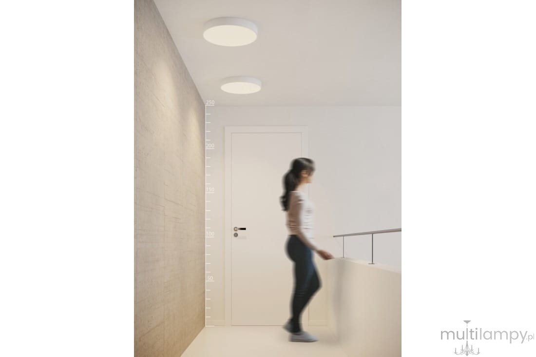 Plafon LED Monza R 40 4000K w kolorze białym, zamontowany na suficie. Okrągły kształt, minimalistyczny design. W tle widoczna ściana z betonu architektonicznego oraz osoba przechodząca w korytarzu.