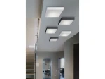 Plafon LED Monza S 22 4000K w kolorze białym, montowany na suficie. Prosty, kwadratowy kształt, z matowym wykończeniem. W tle widoczne inne plafony w ciemniejszych odcieniach. Oświetlenie w nowoczesnym wnętrzu.