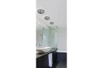 Oprawa sufitowa Erika 1-punktowa w kolorze chromu, zamontowana w łazience. Widoczna z góry, elegancka forma z dekoracyjnym wzorem. Tło jasne, minimalistyczne wnętrze z lustrem, umywalką i ciemnymi szafkami.