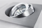 Oprawa sufitowa Editta, 1-punktowa, wykonana z aluminium. W kształcie kwadratu z okrągłym wnęką na żarówkę. Wykończenie w matowym aluminium, z widocznym reflektorem. Produkt zamontowany w pozycji poziomej. Tło neutralne, jasne.