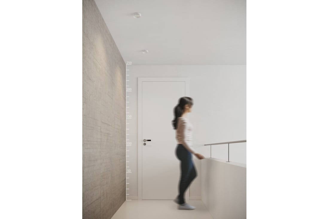 Torres GU10, biała oprawa sufitowa do zabudowy 1-punktowa, zamontowana w sufit. Widoczne detale, w tym gładka powierzchnia i minimalistyczny design. Osoba w tle przechodzi obok otwartych drzwi, w jasnym wnętrzu z betonową ścianą.