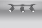 Trzypunktowa lampa sufitowa Merida w kolorze szarym. Elementy o prostej, geometrycznej formie zamontowane na płaskim stelażu. Każdy z reflektorów skierowany w różne strony, emitując światło. Tło jednolite, jasne.