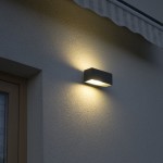 Kinkiet elewacyjny Zen ZN-K100 w kształcie prostokąta, w kolorze czarnym, zamontowany na jasnej ścianie. Emituje ciepłe światło, tworząc efektowne oświetlenie otoczenia. Widok z boku, zbliżony na detal montażu.