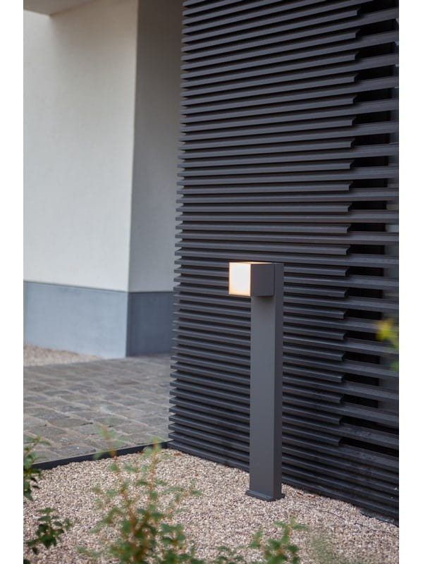 Lampa stojąca ogrodowa Cuba LED H75 w ciemnoszarym kolorze, z regulowanym źródłem światła. Ustawiona na kamiennym podłożu, obok teksturowanej ściany. Prosty, nowoczesny design z kwadratowym kloszem.