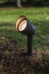 Regulowana lampa stojąca ogrodowa Explorer LED H43 w ciemnoszarym kolorze. Ujęcie z bliska, pokazujące zaokrągloną głowicę emitującą światło, umocowaną na prostym stojaku, osadzoną w trawie. Kabel zasilający widoczny w tle.