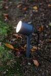 Lampa stojąca ogrodowa Explorer LED H43 w kolorze ciemnoszarym, z regulowanym reflektorem. Ustawiona na ziemi, z widocznym kablem. W otoczeniu trawy i opadłych liści. Idealna do oświetlenia przestrzeni zewnętrznej.