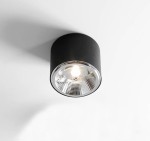 Czarna lampa sufitowa spot 1-punktowa z metalowym kloszem. Ujęcie z dołu, pokazujące zaokrąglony kształt i wewnętrzne wykończenie reflektora. Lampa zamontowana na białym suficie, włączona, emitująca ciepłe światło.