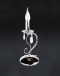 Lampa stołowa Velio 1-punktowa O1958 CH o chromowanej podstawie i cienkiej, zakrzywionej konstrukcji. Posiada przezroczystą, stylizowaną żarówkę w kształcie płomienia oraz wiszące kryształowe zdobienia. Ujęcie frontalne na ciemnym tle.