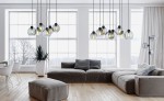 Lampa wisząca Cubus Graphite, 8-punktowa, z przezroczystymi kloszami w kształcie kul, zawieszona na czarnych przewodach. Produkty w aranżacji nowoczesnego wnętrza z dużymi oknami, jasnymi ścianami i drewnianą podłogą.