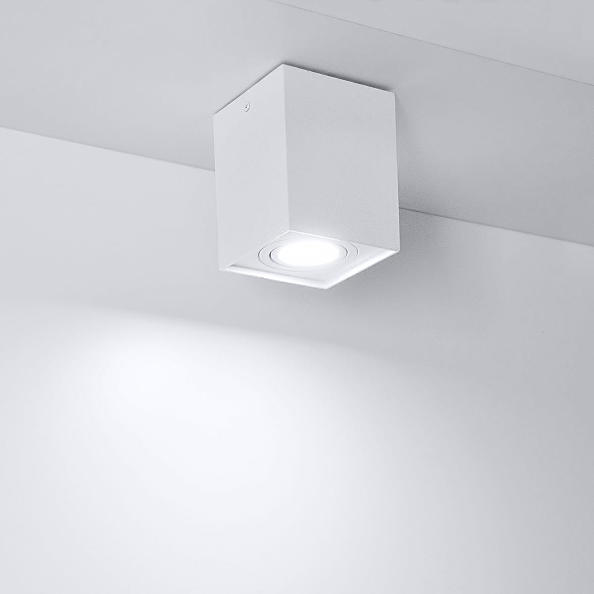 Biała lampa sufitowa kierunkowa Hadar z jedną oprawą GU10, w kwadratowej obudowie. Ujęcie z dołu, lampa zamontowana na suficie. Oświetlenie skierowane w dół, na gładkim, jasnym tle.