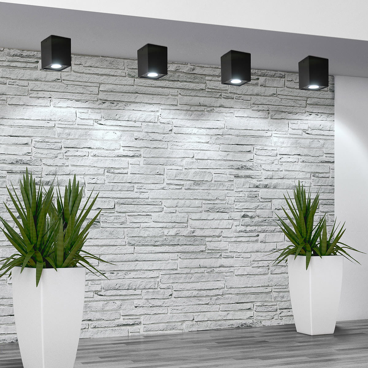 Lampa sufitowa kierunkowa Hadar w kolorze czarnym z jednym gniazdem GU10, zamontowana na białym tle z kamiennej ściany. W tle widoczne rośliny w białych donicach, podkreślające nowoczesny styl aranżacji wnętrza.