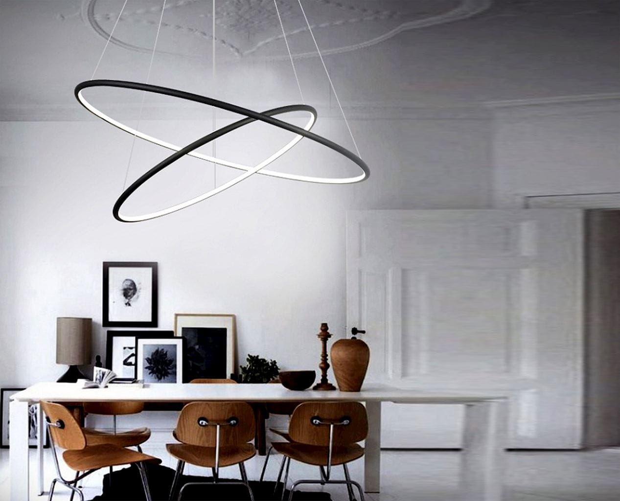 Czarna lampa wisząca Orion LED 2-punktowa z dwoma okrągłymi pierścieniami, jeden w kolorze czarnym, a drugi w białym, zawieszona na cienkich linkach w minimalistycznym wnętrzu. Lampa umieszczona nad drewnianym stołem z krzesłami.