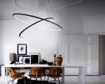 Czarna lampa wisząca Orion LED 2-punktowa z dwoma okrągłymi pierścieniami, jeden w kolorze czarnym, a drugi w białym, zawieszona na cienkich linkach w minimalistycznym wnętrzu. Lampa umieszczona nad drewnianym stołem z krzesłami.
