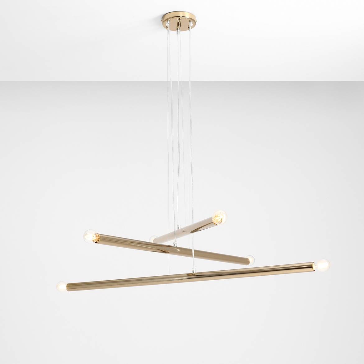 Lampa wisząca Tubo 6-punktowa w kolorze złotym, składająca się z trzech poziomych, prostokątnych rur, z widocznymi żarówkami na końcach. Zawieszona na cienkich linkach z sufitu, prezentuje nowoczesny design na białym tle.