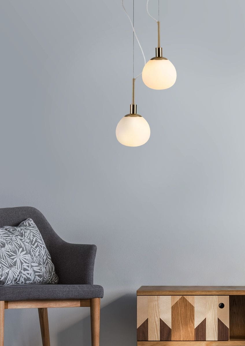 Lampa wisząca Erich MOD221-PL-01-N w kolorze niklu z białymi, okrągłymi kloszami. Zawieszona na cienkich linkach, w aranżacji z szarym fotelem i drewnianą komodą. Klosze emitują miękkie światło, nadając przestrzeni nowoczesny charakter.