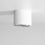 Biała lampa sufitowa spot 1-punktowa, cylindryczna, z metalicznym wykończeniem na dolnej krawędzi. Zamontowana na suficie, prezentuje minimalistyczny design, idealna do oświetlenia wnętrz.