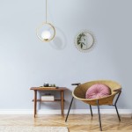 Lampa wisząca Vienna 1-punktowa MLP5573 w złotym okręgu z białym kloszem, zawieszona nad drewnianym stolikiem. Tło w pastelowym odcieniu, w aranżacji z krzesłem i lustrem, tworzy nowoczesny, minimalistyczny wygląd.
