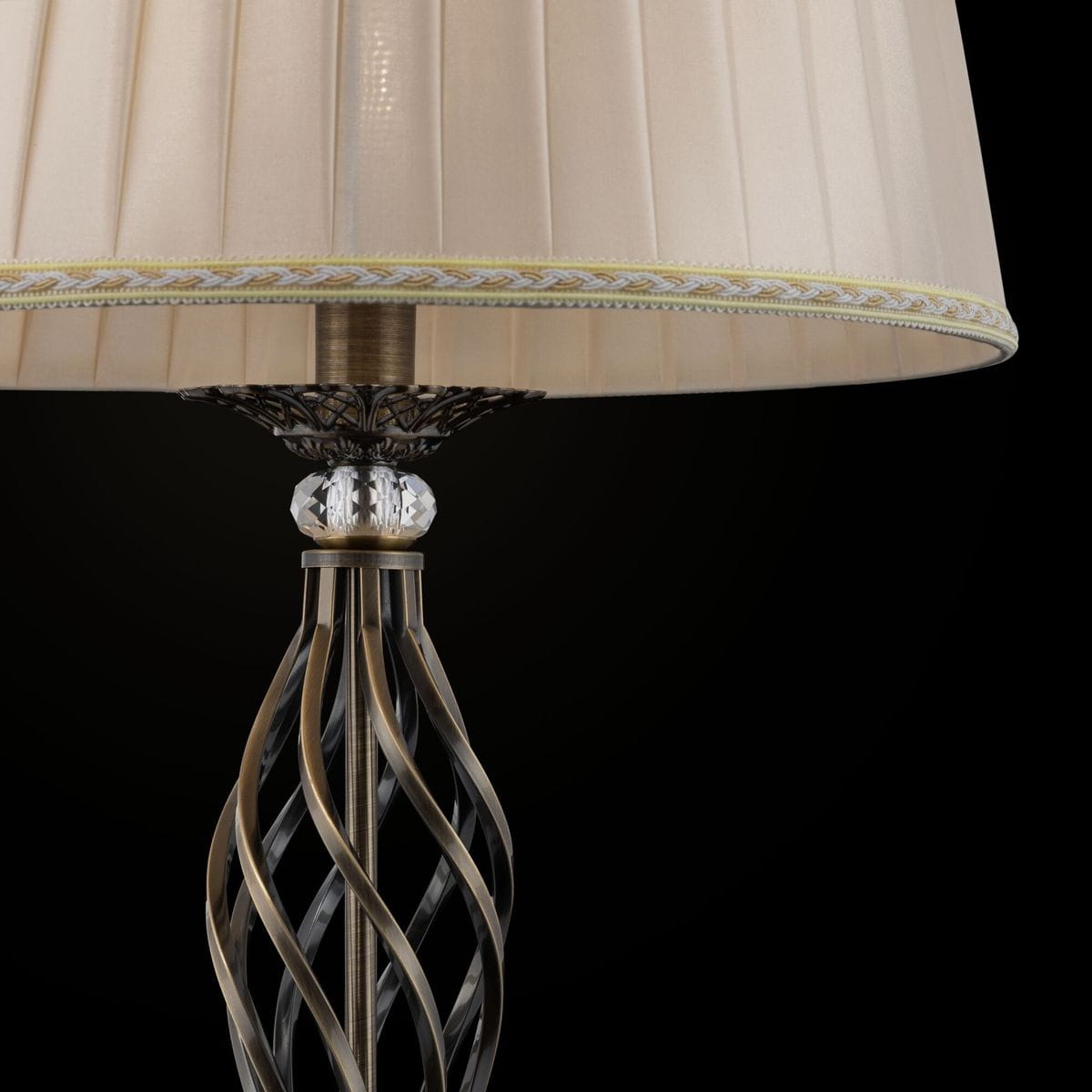 Lampa podłogowa Grace w kolorze patynowym z abażurem w odcieniu kremowym. Podstawa ma dekoracyjny, spiralny kształt oraz kryształowy detal u podstawy. Abażur wykończony złotą taśmą, prezentowany na czarnym tle.