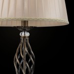 Lampa podłogowa Grace w kolorze patynowym z abażurem w odcieniu kremowym. Podstawa ma dekoracyjny, spiralny kształt oraz kryształowy detal u podstawy. Abażur wykończony złotą taśmą, prezentowany na czarnym tle.