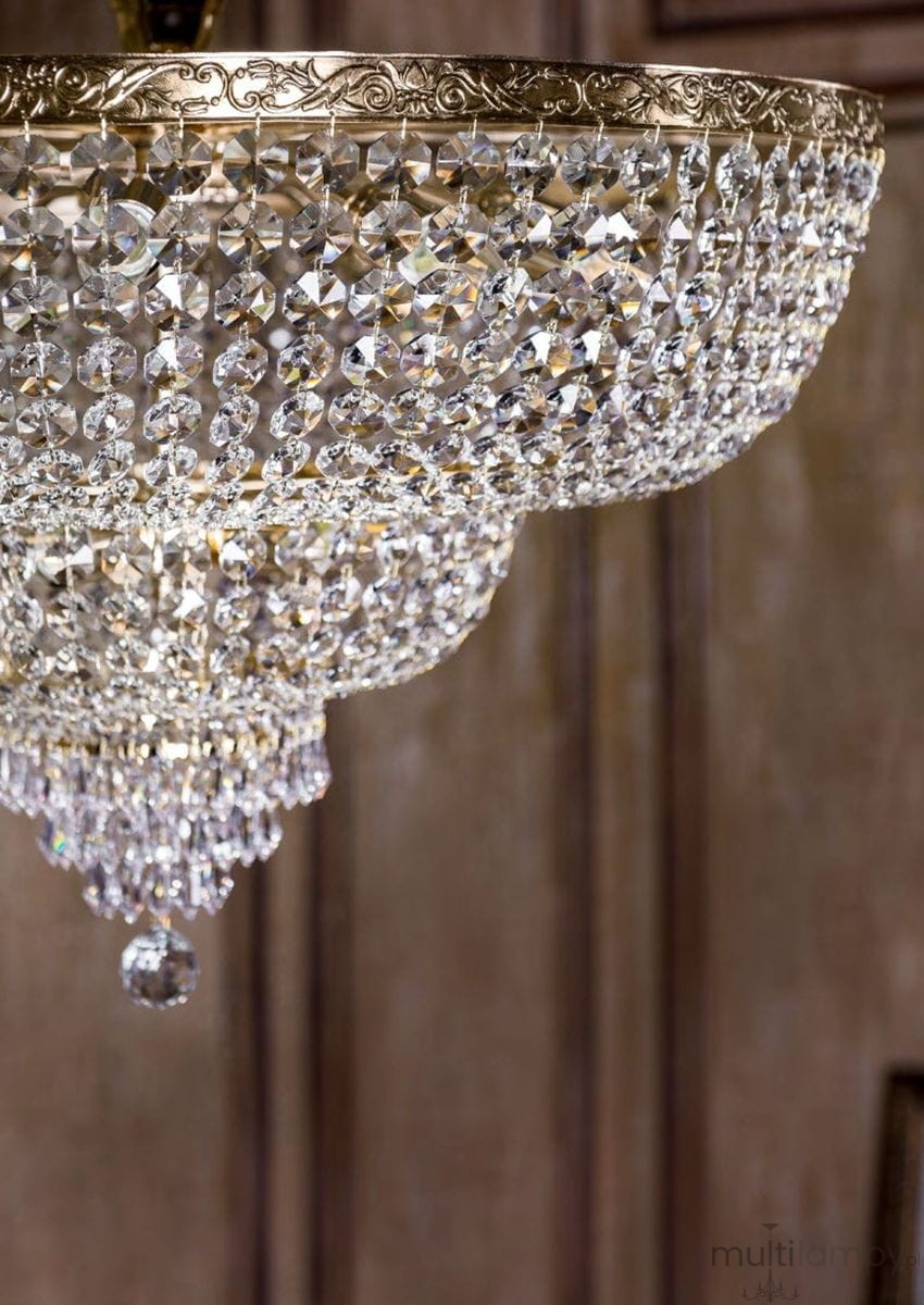 Lampa sufitowa Palace 18-punktowa, złota z kryształowymi wiszącymi detalami. Ujęcie z dołu, pokazujące eleganckie kryształy w kształcie kul oraz ornamentowaną podstawę. Tło w odcieniach brązu, podkreślające blask lampy.