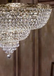 Lampa sufitowa Palace 18-punktowa, złota z kryształowymi wiszącymi detalami. Ujęcie z dołu, pokazujące eleganckie kryształy w kształcie kul oraz ornamentowaną podstawę. Tło w odcieniach brązu, podkreślające blask lampy.