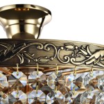 Lampa sufitowa Palace 5-punktowa z ozdobnym złotym abażurem i detalami w stylu roślinnym. Zawieszone kryształowe elementy w kształcie ośmiokątów odbijają światło, tworząc efektowną iluminację. Produkt montowany na suficie.