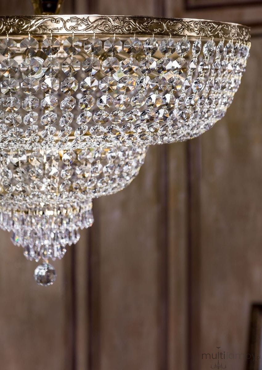 Lampa sufitowa Palace z 14 punktami świetlnymi, o okrągłym kształcie, z metalową, złotą oprawą i dekoracją z kryształowych elementów, zawieszone na cienkich łańcuszkach. Widoczny detal w postaci kulistego kryształu na dole.