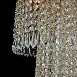 Lampa sufitowa Cascade 12-punktowa z kryształowymi zdobieniami w kształcie diamentów, zawieszona na złotych łańcuszkach. Widoczna jest tekstura kryształów, które odbijają światło, tworząc efekty świetlne. Kąt ujęcia z boku, na czarnym tle.