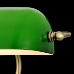 Lampka stołowa Kiwi Z153-TL-01-BS z zielonym kloszem z przezroczystego szkła, metalową podstawą w kolorze mosiądzu i regulatorem. Klosz ma zaokrąglony kształt, a całość prezentuje się na czarnym tle.