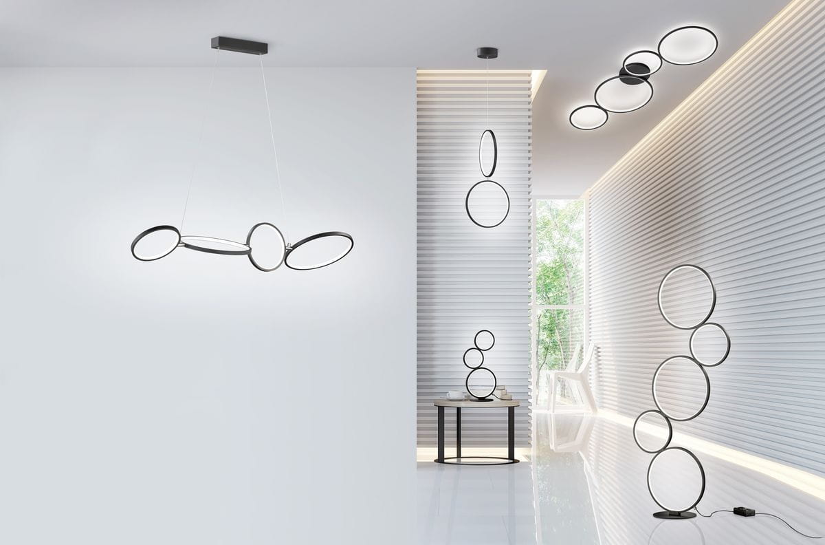 Czarna lampa sufitowa Rondo LED 4-punktowa z okrągłymi kloszami, zamontowana na prostokątnym stelażu. Widoczna w nowoczesnym wnętrzu, w towarzystwie innych lamp w formie okręgów na ścianach. Jasne tło podkreśla minimalistyczny design.
