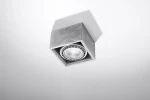 Lampa sufitowa Quatro 1-punktowa w betonowej obudowie, kwadratowy kształt. Zainstalowana na suficie, widoczny reflektor w centrum. Szara faktura betonu, minimalistyczny design, podkreśla nowoczesne wnętrza.
