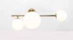 Złota lampa sufitowa Dione 3-punktowa z trzema białymi, okrągłymi kloszami w matowym wykończeniu. Ujęcie frontalne, lampa zamontowana na suficie, z prostą konstrukcją. Klosze umieszczone na różnych wysokościach, wykonane z szkła.