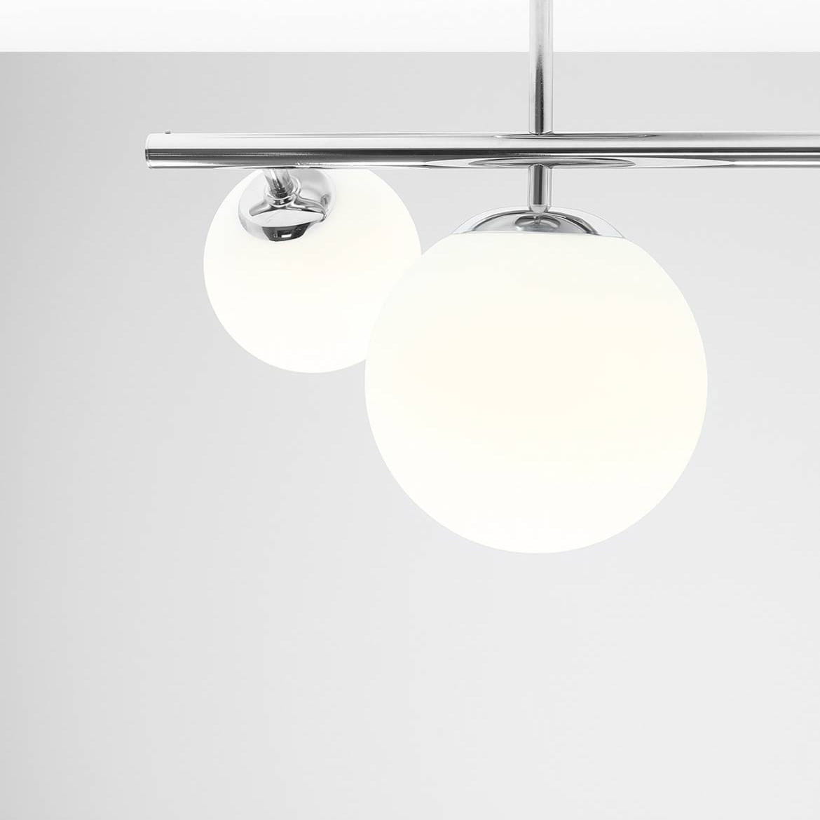 Lampa sufitowa Dione 3-punktowa w kolorze chromu z dwoma białymi, okrągłymi kloszami z mlecznego szkła. Ujęcie z góry, ukazujące detale konstrukcji oraz przezroczystość kloszy. Zawieszona na prostym stelażu.