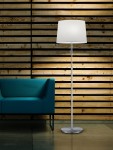 Lampa podłogowa Lyon 3-punktowa, niklowana, z białym abażurem, stojąca obok niebieskiej sofy. Ujęcie z boku, na tle drewnianej ściany. Wysoka, prosta konstrukcja z okrągłą podstawą.