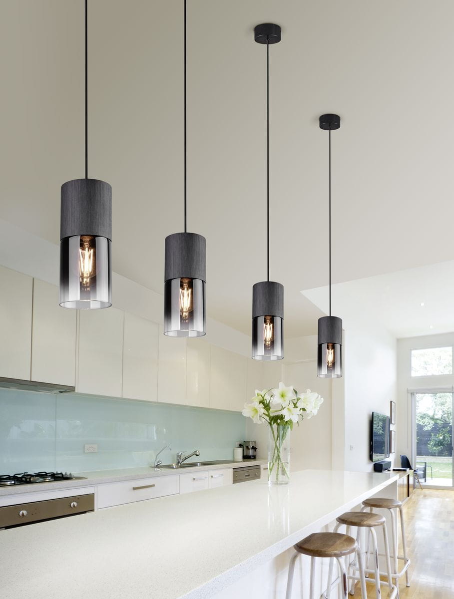 Lampa wisząca Robin 1-punktowa w kolorze czarnym z metalowym kloszem i przezroczystym wykończeniem, zawieszona na długim przewodzie, umieszczona nad jasnym blatem w nowoczesnej kuchni. W tle widać białe meble i bukiet białych kwiatów.