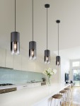 Lampa wisząca Robin 1-punktowa w kolorze czarnym z metalowym kloszem i przezroczystym wykończeniem, zawieszona na długim przewodzie, umieszczona nad jasnym blatem w nowoczesnej kuchni. W tle widać białe meble i bukiet białych kwiatów.