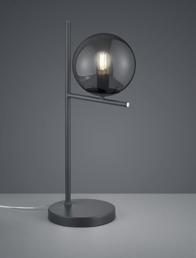Lampa stołowa Pure 1-punktowa w kolorze antracytowym. Posiada okrągły klosz z ciemnego szkła oraz prostą, metalową podstawę. Ujęcie frontalne, lampa stoi na płaskiej powierzchni, z widocznym przewodem.