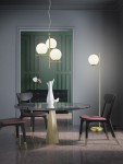Lampa podłogowa Pure 1-punktowa, wykonana z mosiądzu, z okrągłą głowicą umieszczoną na smukłym stelażu. Ujęcie z boku, lampa stoi obok okrągłego stołu w eleganckim wnętrzu. Tło w stonowanych odcieniach szarości i zieleni.