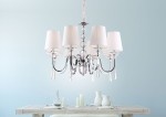 Żyrandol Charlotte 8-punktowy, chromowana konstrukcja z białymi abażurami, wiszący w centralnej części zdjęcia. Delikatne kryształowe detale, osiem ramion, elegancki design. Tło w delikatnym błękicie, stół z białymi naczyniami w aranżacji.