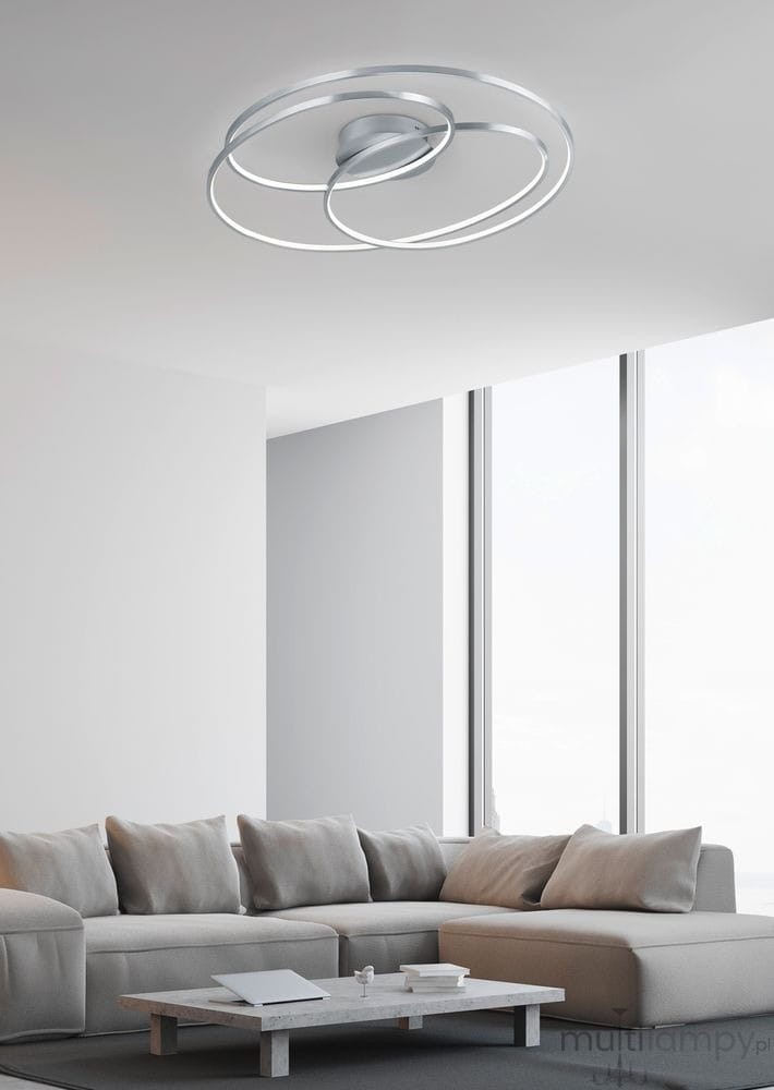 Lampa sufitowa Gale LED 1-punktowa w kolorze niklowym, z nowoczesnym, okrągłym kształtem. Zamontowana na suficie, w jasnym wnętrzu z dużymi oknami. Widziana z dołu, ukazuje dwa splecione pierścienie, emitujące równomierne światło.