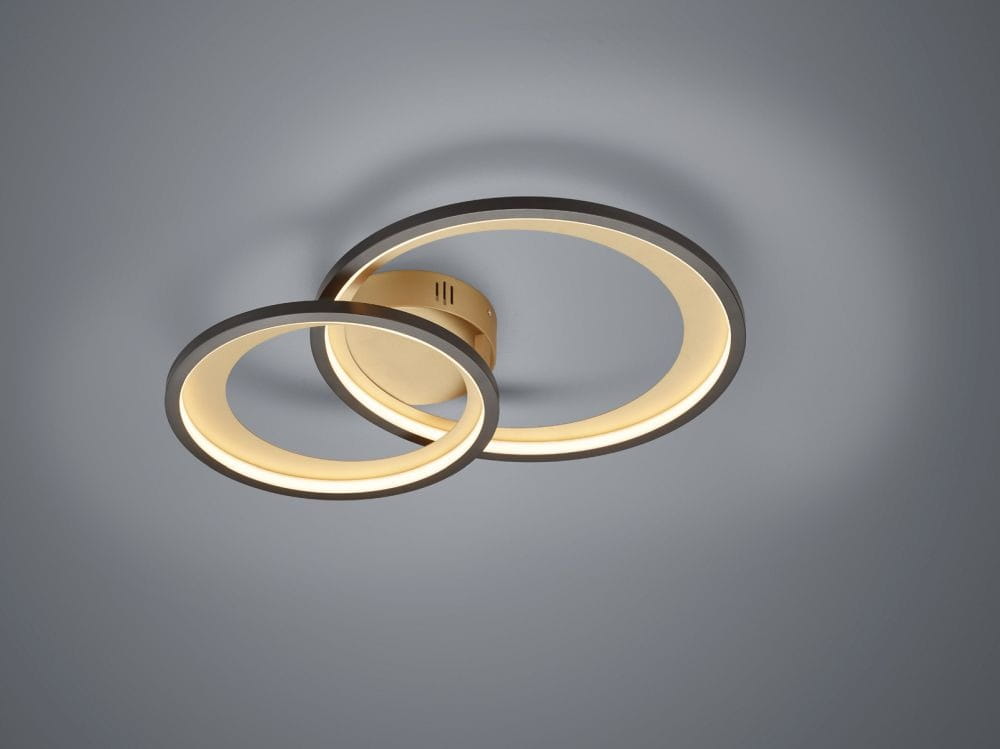 Czarna i złota lampa sufitowa LED 2-punktowa, składająca się z dwóch nachylonych, okrągłych pierścieni emitujących ciepłe światło. Produkt zamontowany na ścianie, z widocznym detalem łączenia. Tło szare, minimalistyczne.