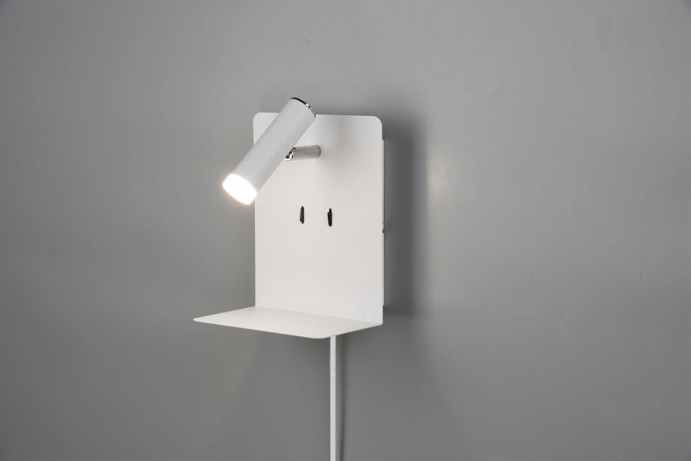 Kinkiet LED w kolorze białym z portem USB, montowany na ścianie. Posiada ruchomą głowicę lampy oraz półkę do odstawienia przedmiotów. Widoczny kabel zasilający, prosta konstrukcja na tle szarej ściany.