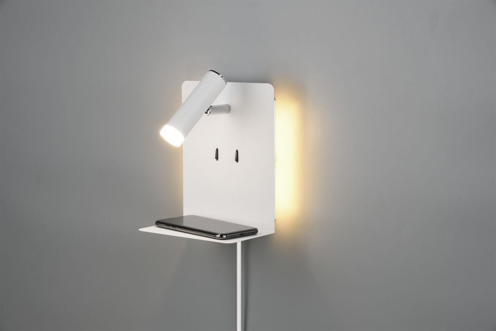 Kinkiet LED w kolorze białym z portem USB, z zamontowanym kloszem w ruchomej pozycji oraz małą półką na telefon. Oświetlenie z tyłu emituje ciepłe światło, a całość jest przymocowana do szarej ściany.