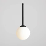 Lampa wisząca Bosso D14, 1-punktowa, z czarnym metalowym uchwytem i białym, okrągłym kloszem. Zawieszona na cienkim kablu, prezentuje minimalistyczny design. Tło jasnoszare, co podkreśla elegancki charakter lampy.